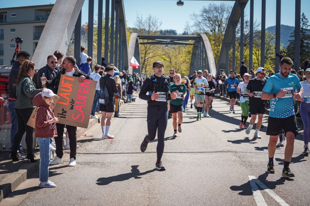 Mehrere Läufer rennen über eine Brücke. Links und rechts feuern Zuschauer die Läufer an.